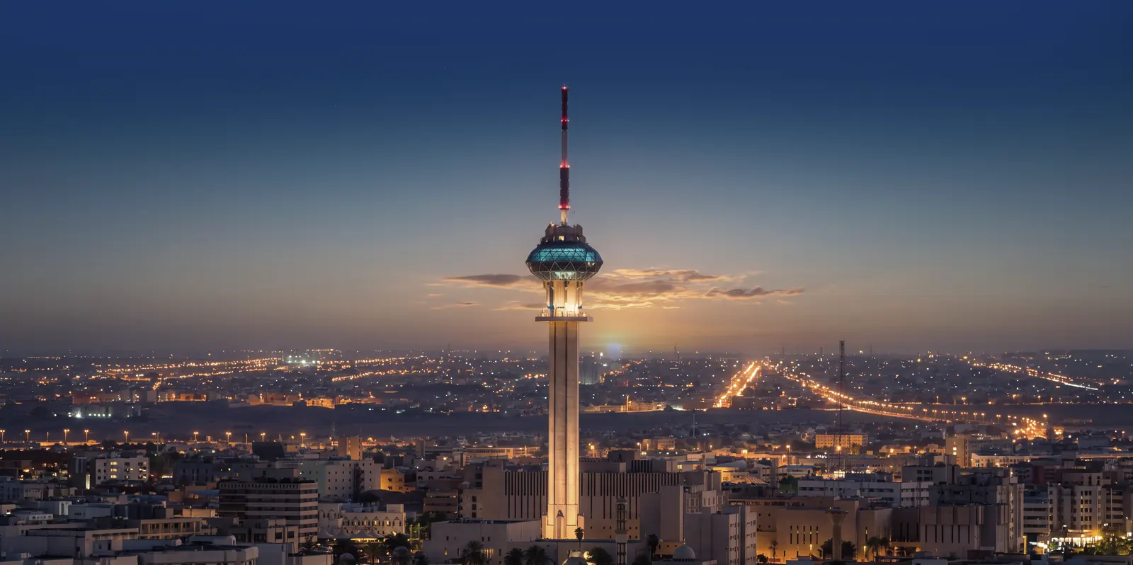 Riyadh at dusk: the TV tower lit against the last of the sunset, the city's lights already on across the plain.