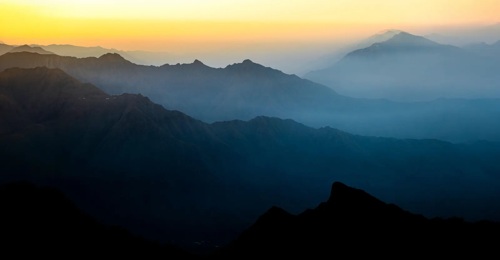 Mountain ranges layered in haze at first light, ridge standing behind ridge and fading into a gold sky.