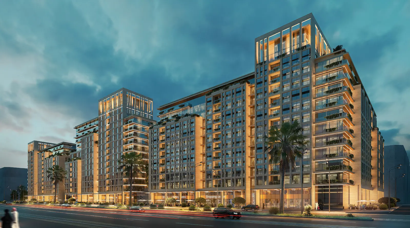 The district at dusk, seen along the boulevard: stepped residential blocks lit from within, above a lit retail podium and moving traffic.